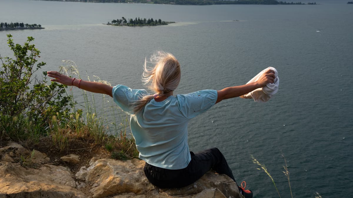 Woman enjoys a breathtaking lake view from a cliff at sunset, exemplifying freedom and adventure.